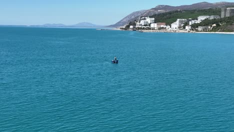 Solo-fisherman-pulls-boat-along-line-in-water-on-sunny-day-near-coast