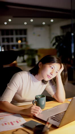 vertical video of asian businesswoman using laptop at office, slow motion