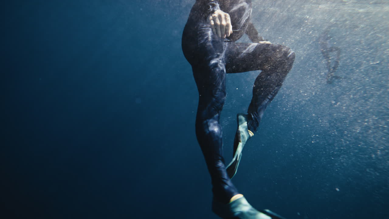 Ben af person i våddragt, der snorkler under vandet nær overfladen i klart hav