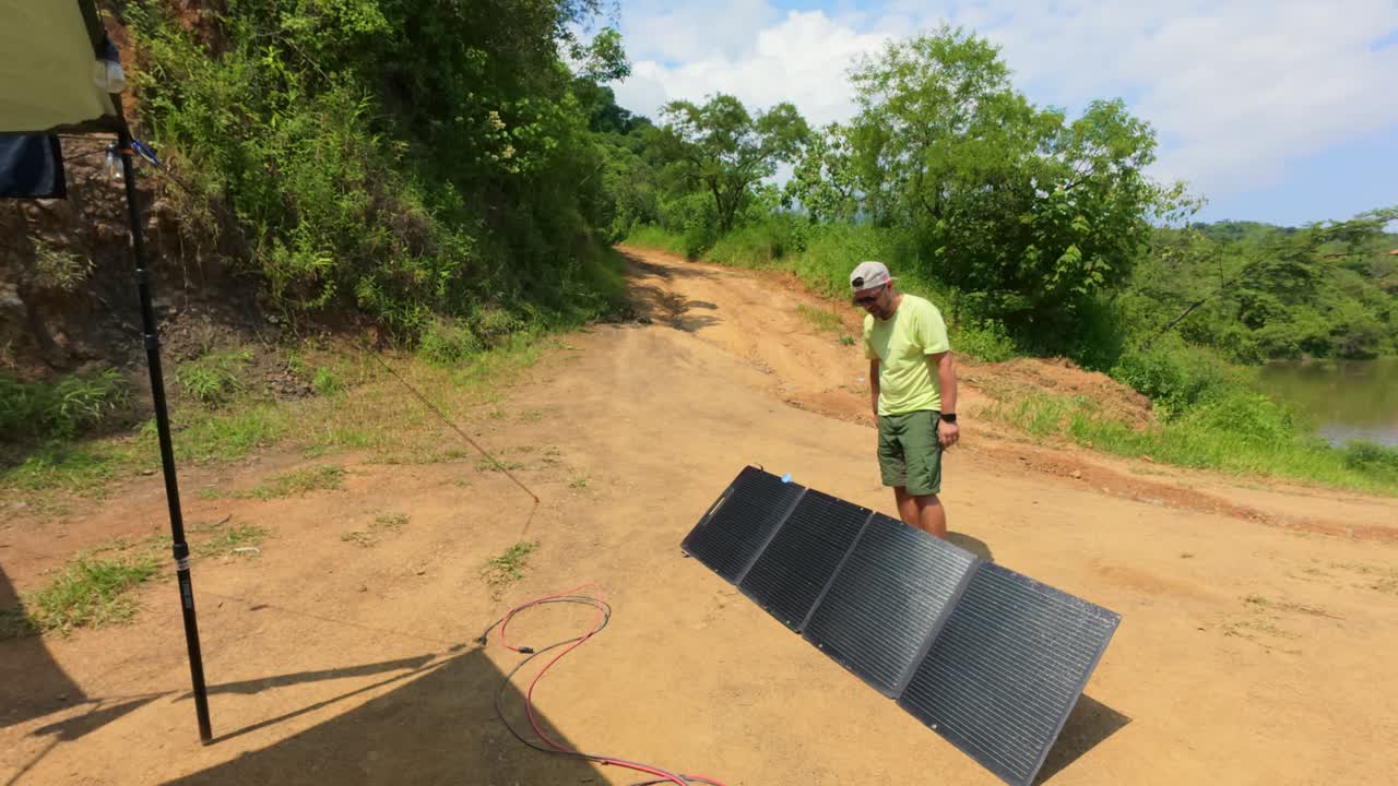 Mand installerer transportable solpaneler på en jordsti nær træer og en sø ved Presa El Carrizo, Mexico