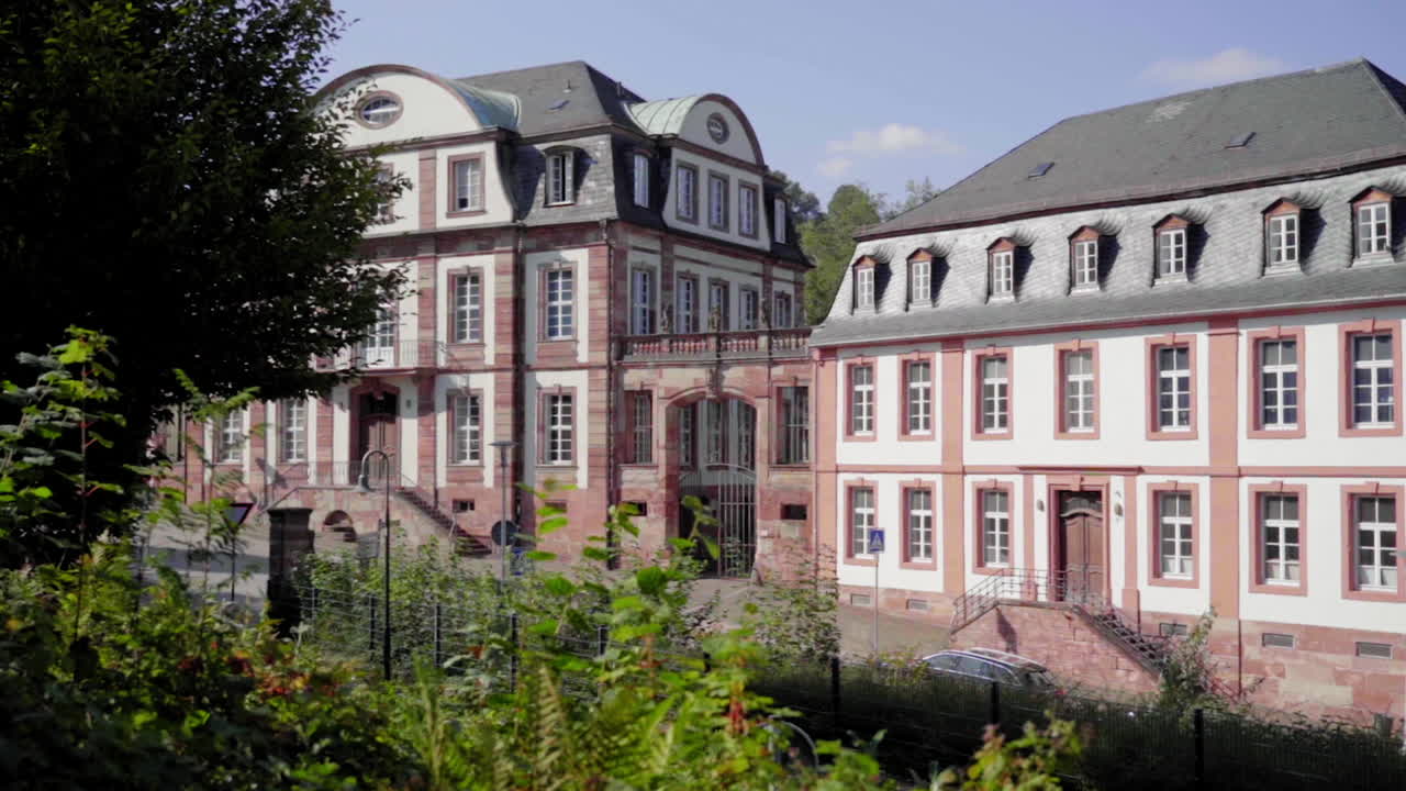 low motion view of the historic Von der Leyen High School in Blieskastel, surrounded by lush greenery and showcasing classic German architecture under the summer sun.