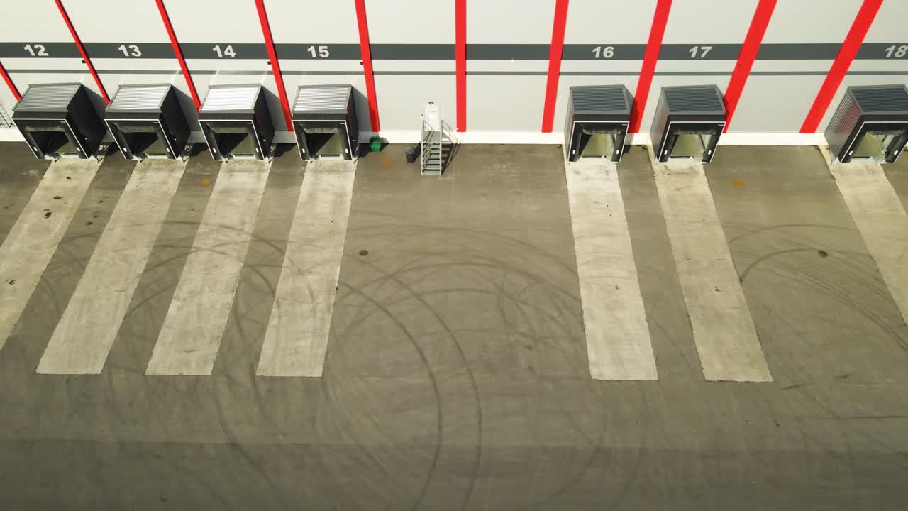 Pohled z dronu prolétávajícího kolem prázdných nakládacích ramp ve velkém moderním distribučním skladu během denních logistických operací