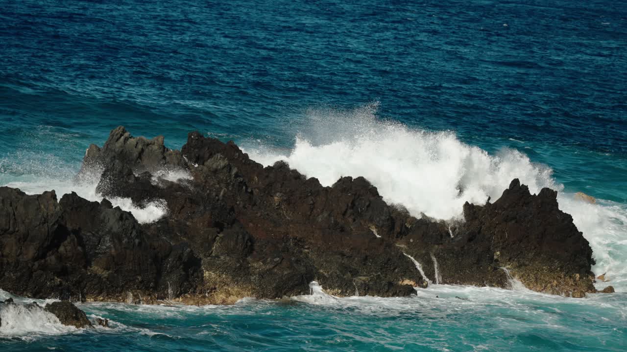 Slow-motion Atlantic wave surges over jagged volcanic coastline in Madeira, misting into the air with a rhythmic burst of seafoam and energy.