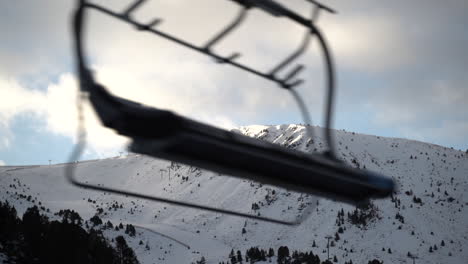 blurred and empty ski lift passing frame with beautiful snowy mountain top view in background at sunset