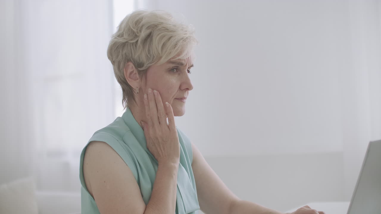 una mujer de edad está trabajando con una computadora portátil en la oficina sintiendo un agudo dolor de muelas tocando y frotando el dolor de mejilla y la incomodidad