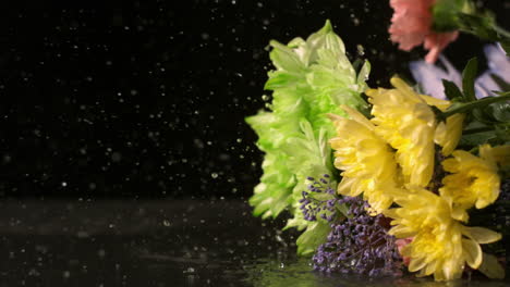 un ramo de flores cayendo sobre una superficie negra y húmeda