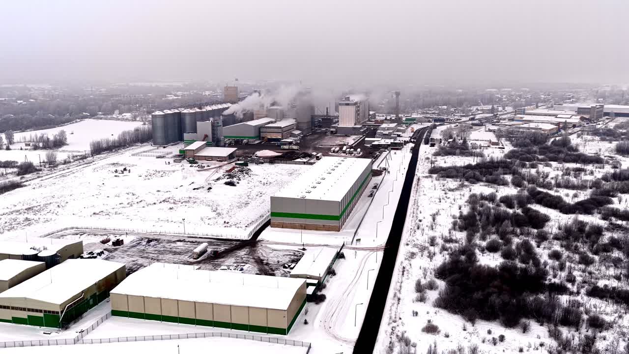 En sirkulerende droneopptak av et aktivt industrianlegg og produksjonsanlegg dekket av dyp snø på en kald vinterdag i Jelgava