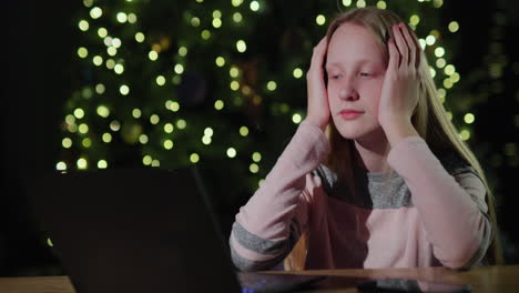 Trauriges-Kind,-Das-Vor-Dem-Hintergrund-Verschwommener-Weihnachtsbaumlichter-Auf-Den-Laptop-Bildschirm-Schaut