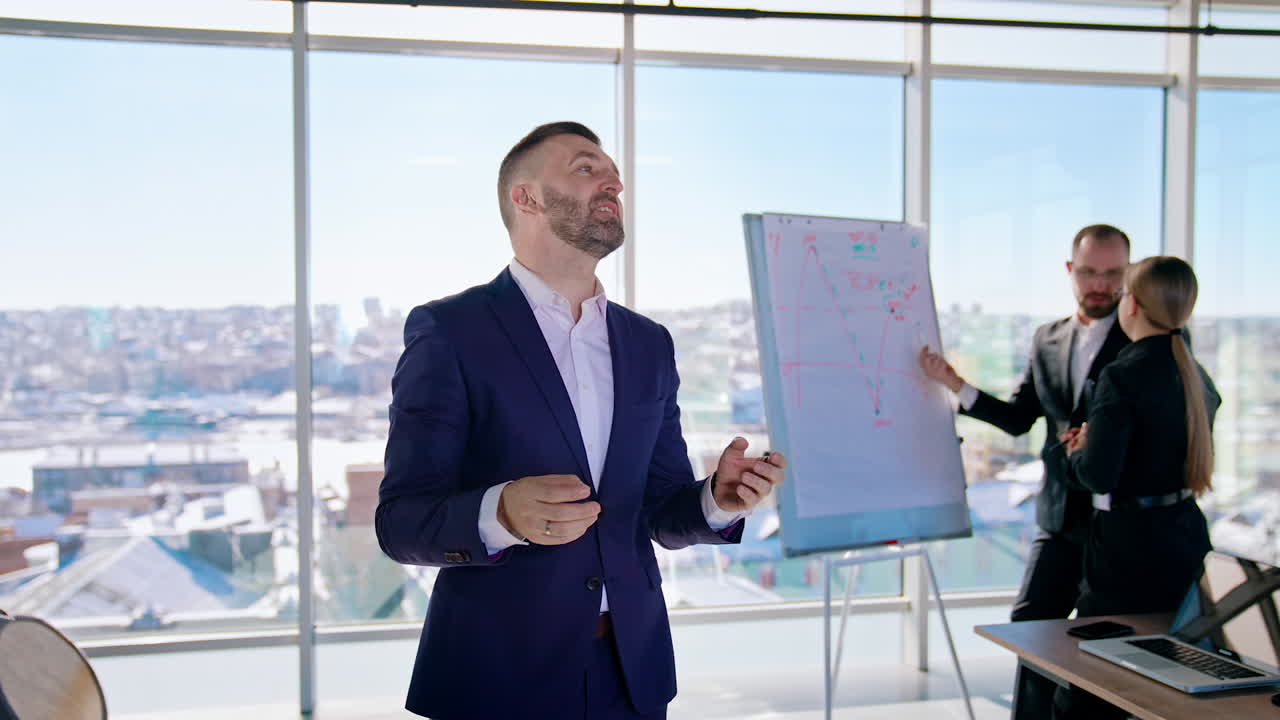 Confident businessman speaking in modern office. Elegant man in costume telling about his success in business on camera. Executive business workers indoors.