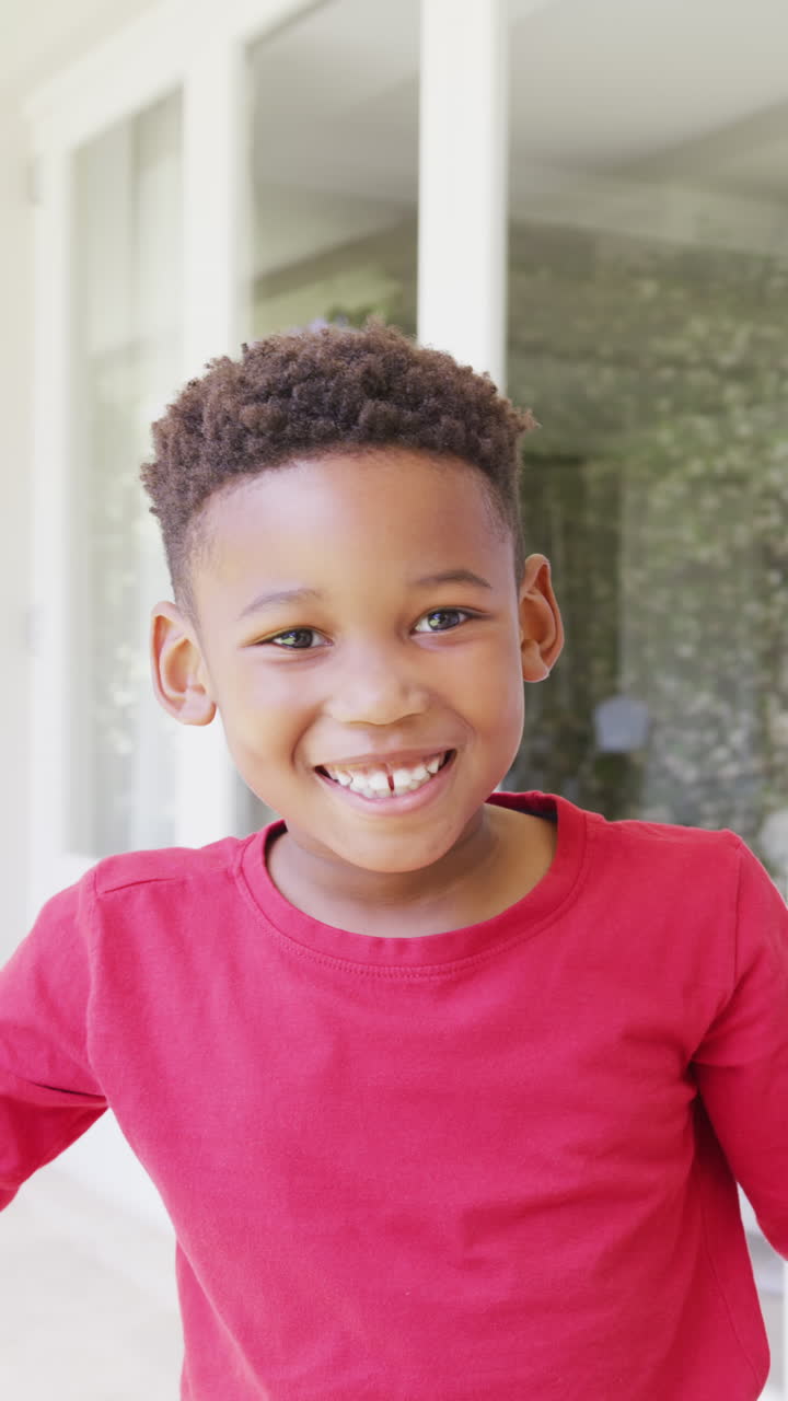 Vertical video of portrait of happy african american boy looking at camera, in slow motion