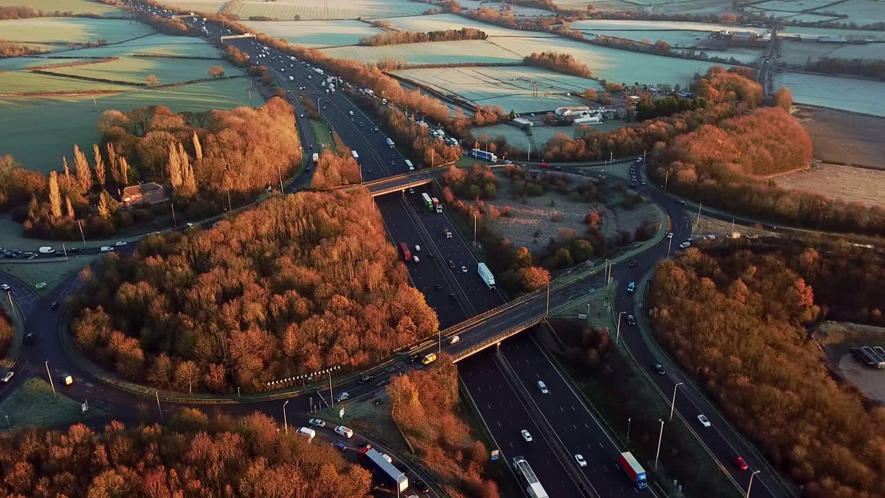 Drone Aerial View Of A Busy Motorway Junction Sliding Right To Left With Cars And Trucks In The Winter With Orange And Brown Trees