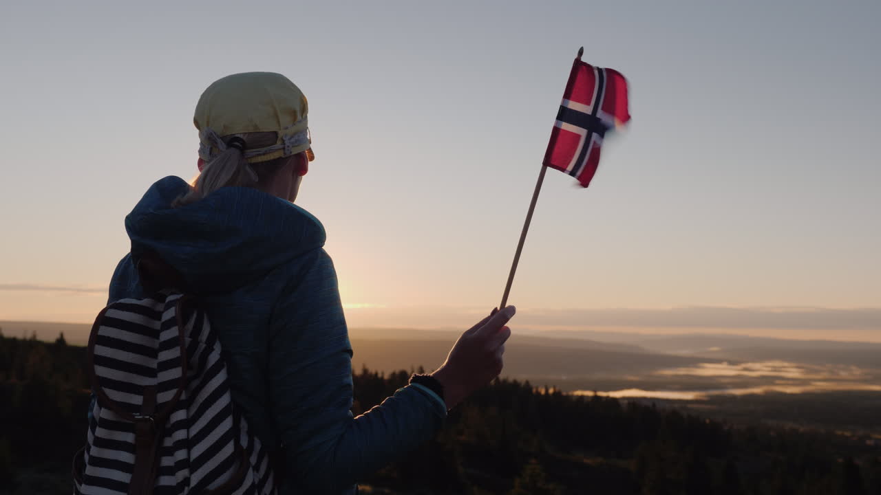 Podróżnik z flagą Norwegii w ręku wita wschód słońca na szczycie góry, ciesząc się chwilą.