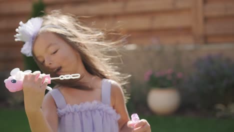 a little girl in a dress is blowing soap bubbles in the backyard on a sunny summer day