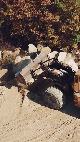 specially equipped machine with a bucket id working near a quarry with stones on the background of sand.. vertical video