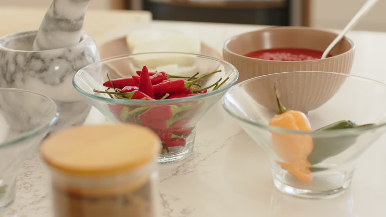 Camera is sliding forward pulling focus across counter and showing red chilies, spice jars for prep