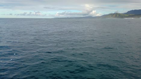 4K-Hawaii-Kauai-Bootfahren-Auf-Dem-Meer,-Das-Von-Rechts-Nach-Links-Schwimmt-Und-Nach-Unten-Geneigt-Ist,-Um-In-Der-Ferne-Die-Wolkige-Küste-Mit-Der-Gischt-Des-Bootes-Im-Vordergrund-Zu-Sehen