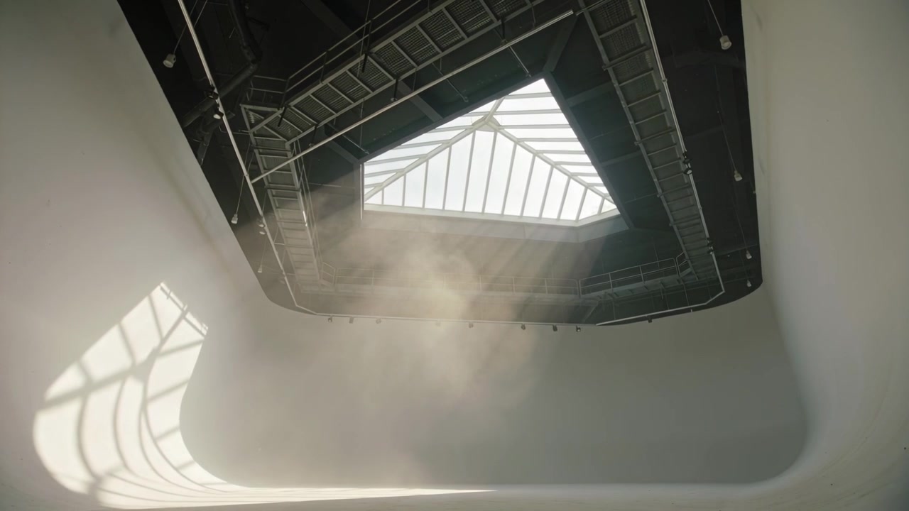 Fascio di luce che filtra attraverso la cornice di un lucernario, polvere che si sposta, diffondendosi nell'aria, proiettando un'ombra a griglia nell'atrio