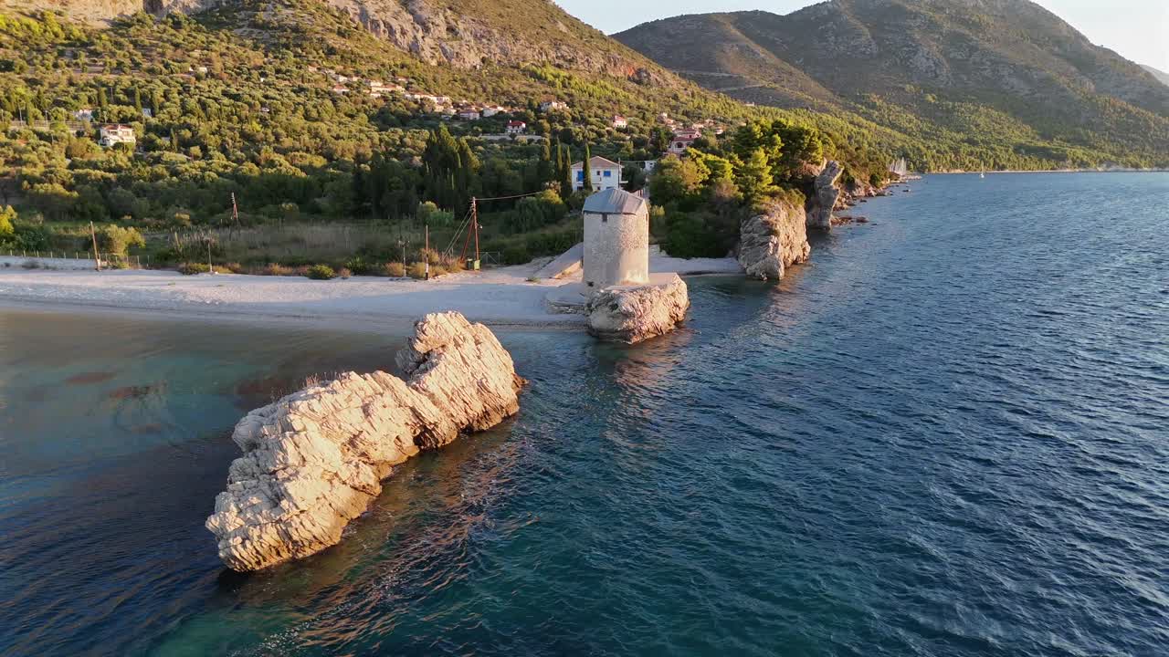 Greece,Kalamos Island,Agrapidia Beach,Aerial view half circle pan right around one and only standing windmill by the beach with sailboats anchored at the back ground.Early in the morning no people