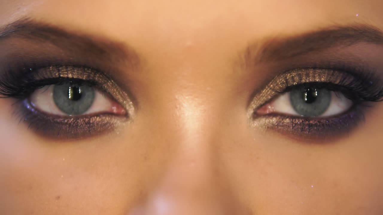 Close Up view of woman's eyes with beautiful golden makeup opening and closing in Slow Motion