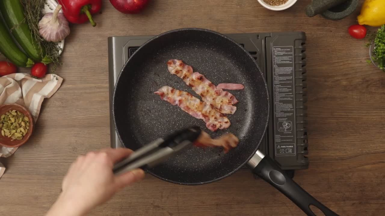 Crop person turning bacon frying in pan