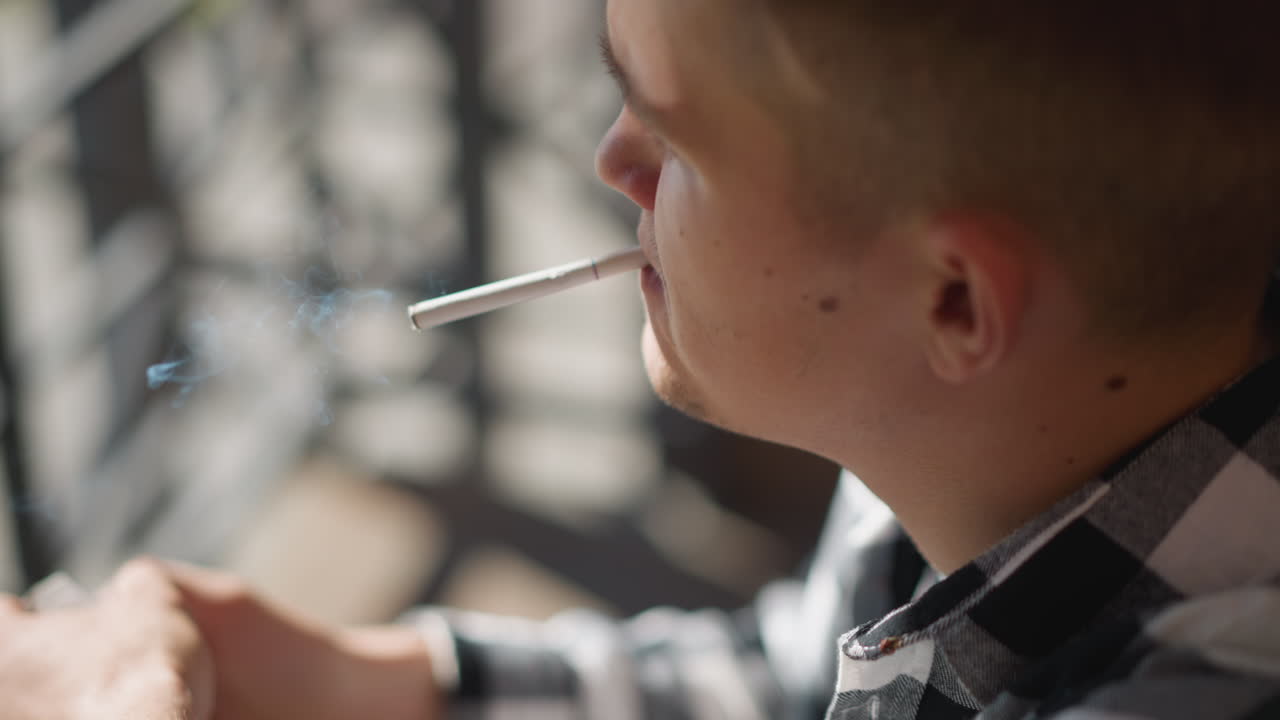 close up of white boy smoking on iron railing outdoors in urban setting soft background blur highlights contemplative mood in warm sunlight