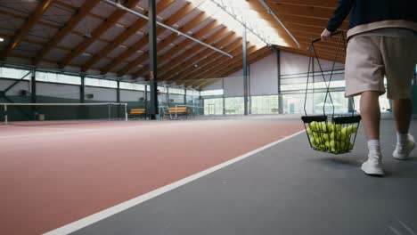 man carrying tennis balls basket on indoor court