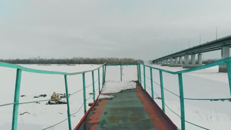 green rusty pier stands at frozen river against large bridge