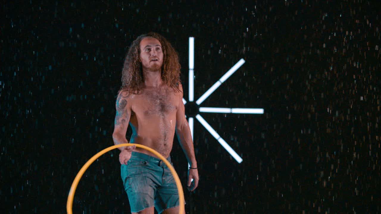 Male hula hooper playing and flinging hula hoop into the air, wet rain studio