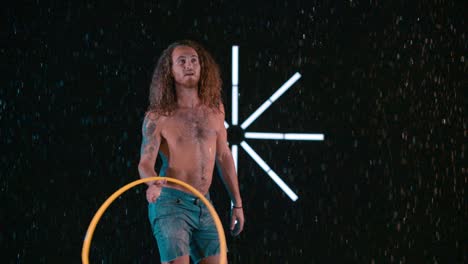 male hula hooper playing and flinging hula hoop into the air, wet rain studio