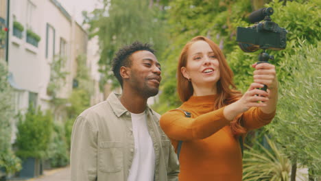 young couple travelling through city together vlogging to video camera in park