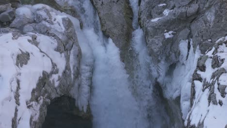 Waterfall-inside-massive-glacier-canyon,-water-falling-through-frame-with-snowy-mountain-wall-background