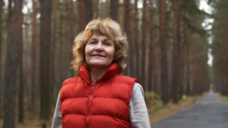 mujer madura sonriente con ropa deportiva mirando la cámara en el bosque