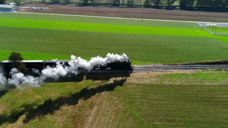 steam passenger train puffing smoke along amish countryside as seen by a drone