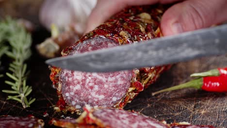 the hand of a man with a knife cut pieces of salami.