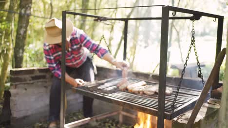 ethnic man preparing raw meat pieces above burning fire