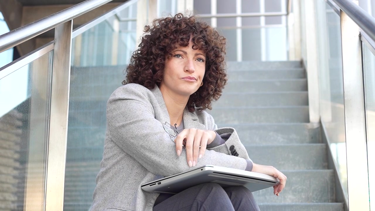 A businesswoman sits on stairs with her laptop contemplating ideas and strategies for success