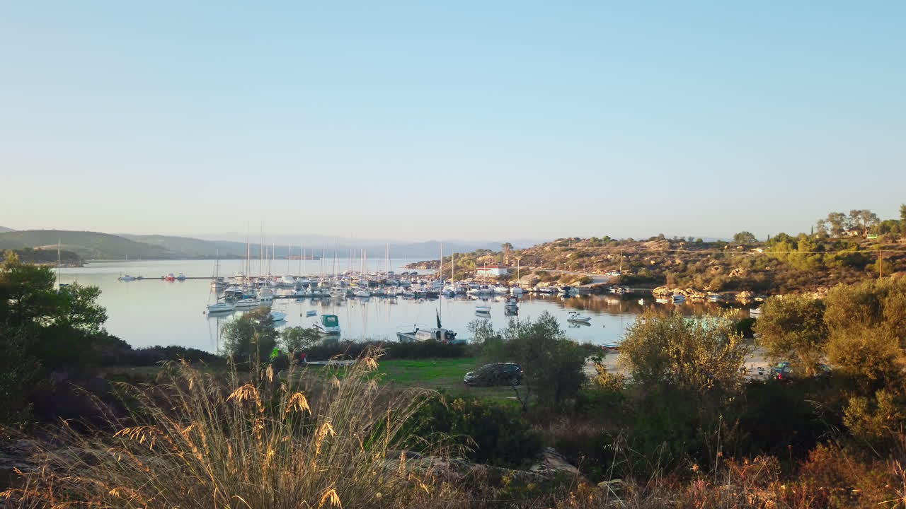 Aegean sea port with multiple moored yachts near piers, greenery, hills around it, Greece. Slow motion