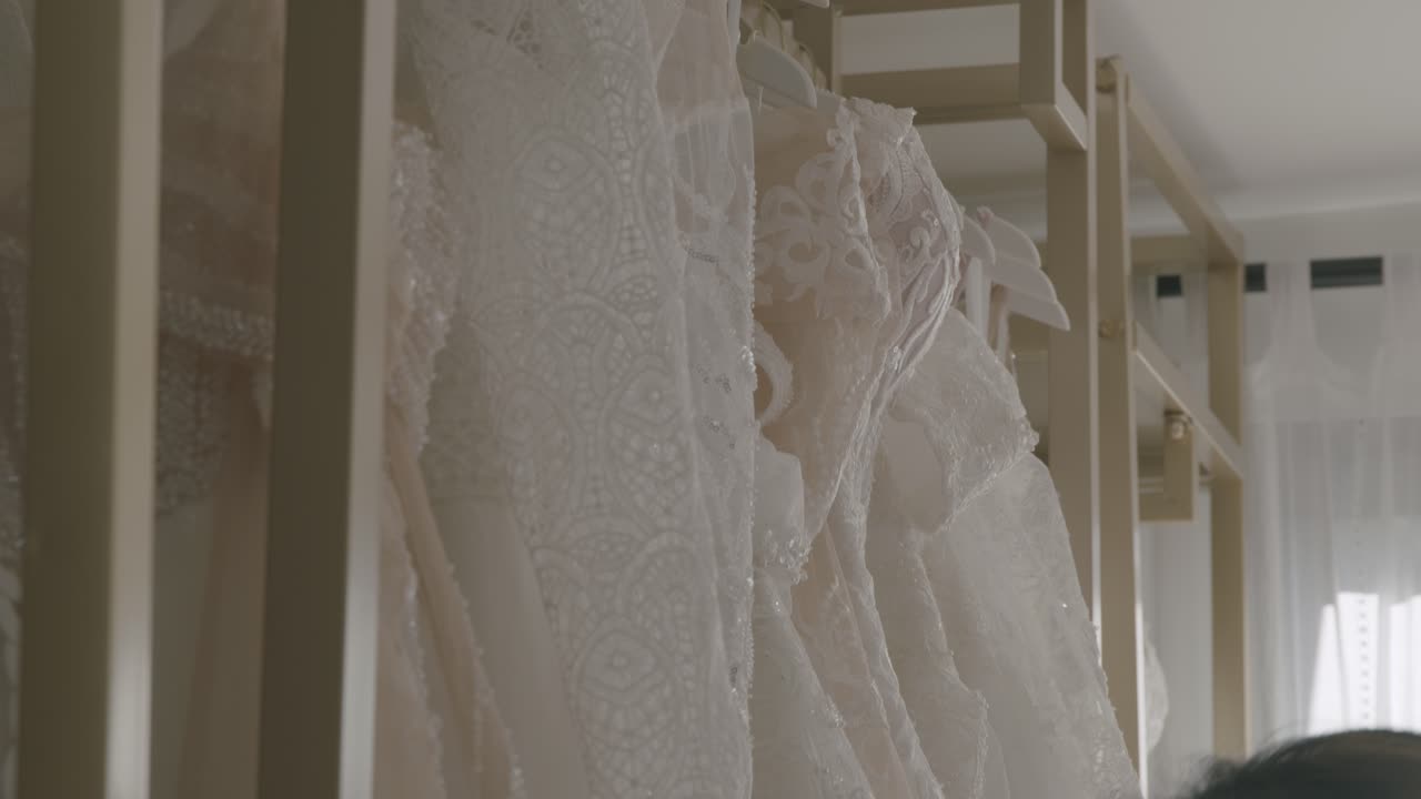 A close-up shot of detailed lace bridal gowns hanging in a boutique, exuding elegance. Soft, natural lighting enhances the delicate textures and intricate design