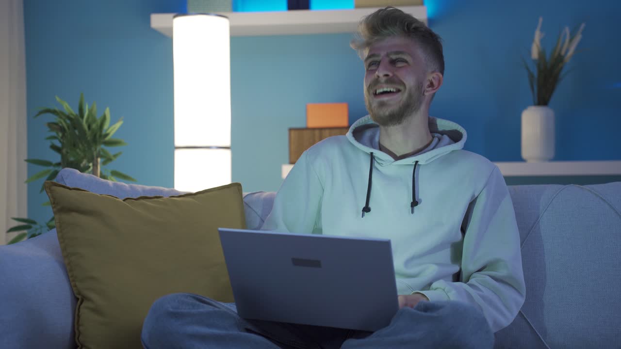 el joven se alegra mientras usa la computadora portátil en casa, las buenas noticias lo hacen feliz y su alegría es restaurada.