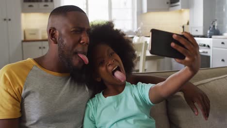 Hija-Afroamericana-Y-Su-Padre-Haciendo-Caras-Tomando-Selfie-Juntos-En-El-Sofá