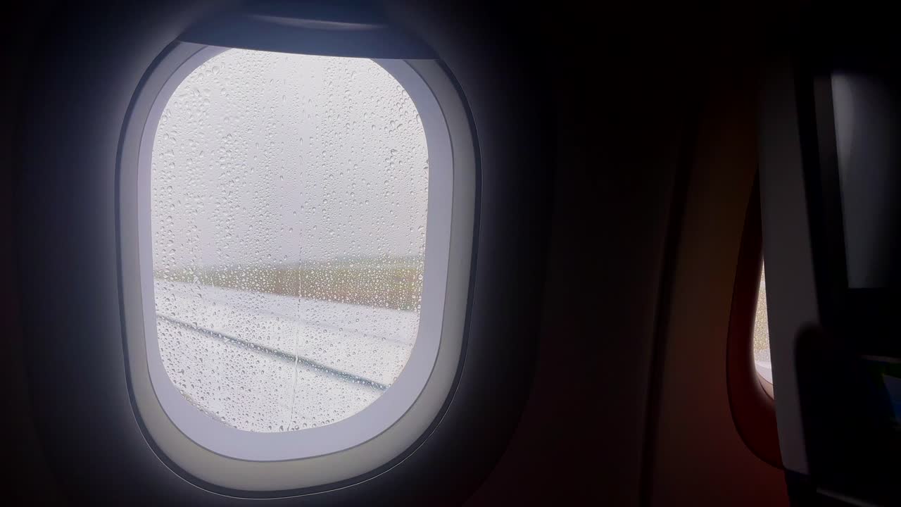 Raindrops on an airplane window with a misty view of the runway in Greece