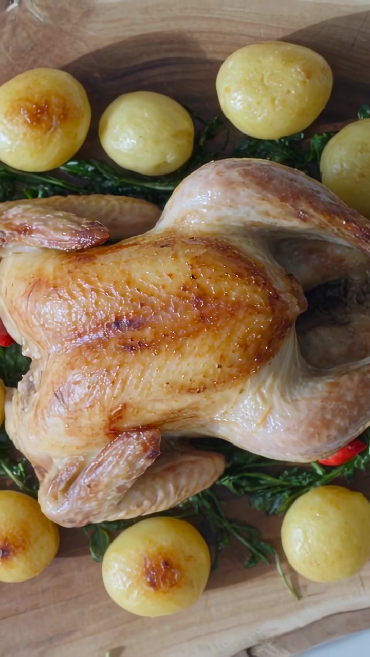 Video verticale: Telecamera che si allontana mostrando un pollo arrosto su un tagliere, rivelando patate e verdure