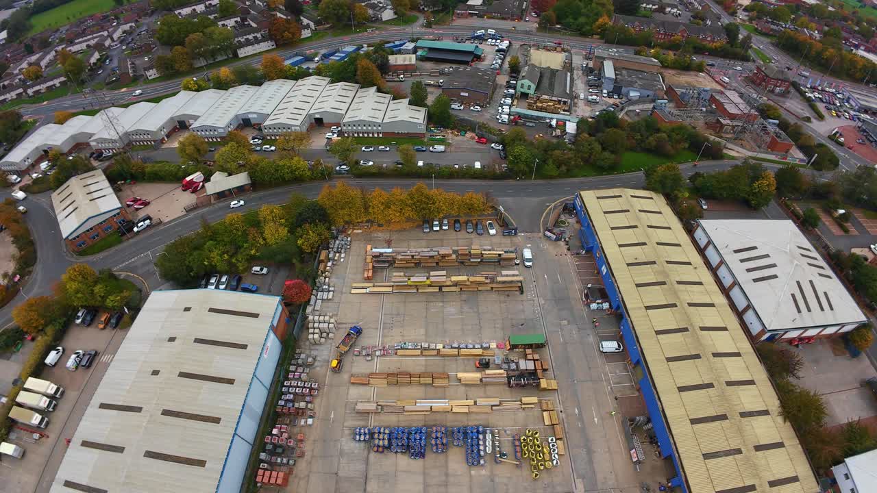 Aerial View Industrial Warehouse Yard Storage, Drone Captures Rooflines, Loading Bays, Parked Trucks, Stacked Containers, Concrete Lot, Adjacent Suburban Roads And Green Trees Overcast Sky Highangle