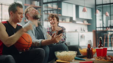 at home three fans on couch watch basketball game on tv, use smartphone app for checking score, online bet, statistics, celebrate when team wins championship. friends watch favourite club play