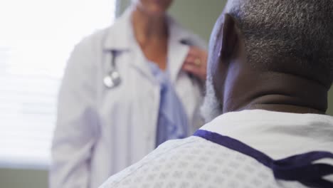 mid section of female doctor talking and supporting african american senior male patient at hospital