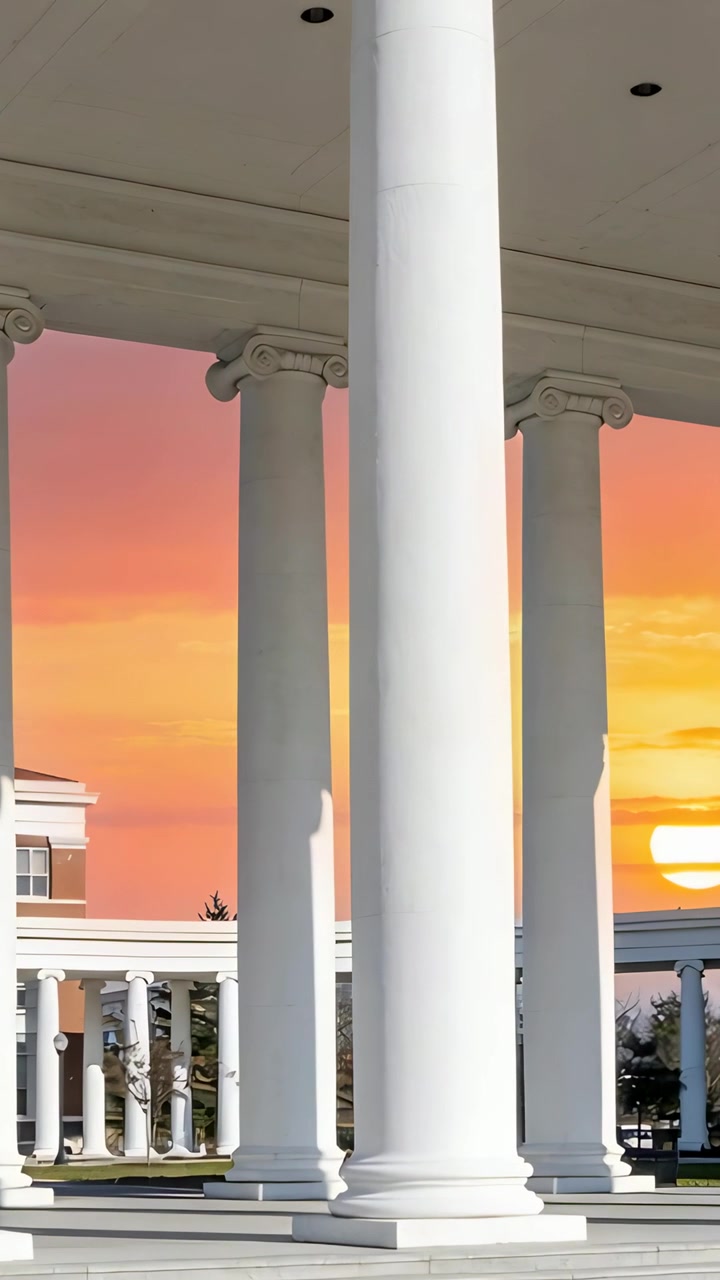 Vertical video: Panning central white column under colonnade, camera framing sunset, capturing glow