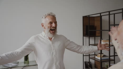 two happy senior men friends greeting each other with a hug and laughing at home 2