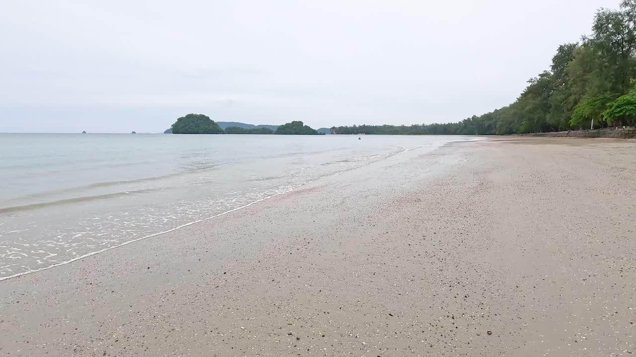 태국 크라비의 조용한 해변 장면, 부드러운 파도와 부드러운 자연 조명 아래 울창한 초록색을 보여줍니다.