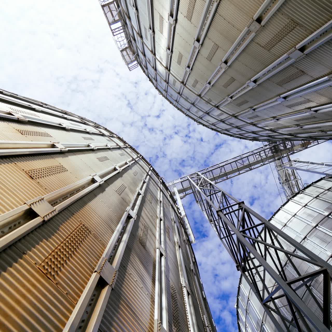 Modern grain terminal. Metal storage tanks for drying grain. Industrial equipment for agribusiness. Large grain elevators on blue sky background. Close-up.