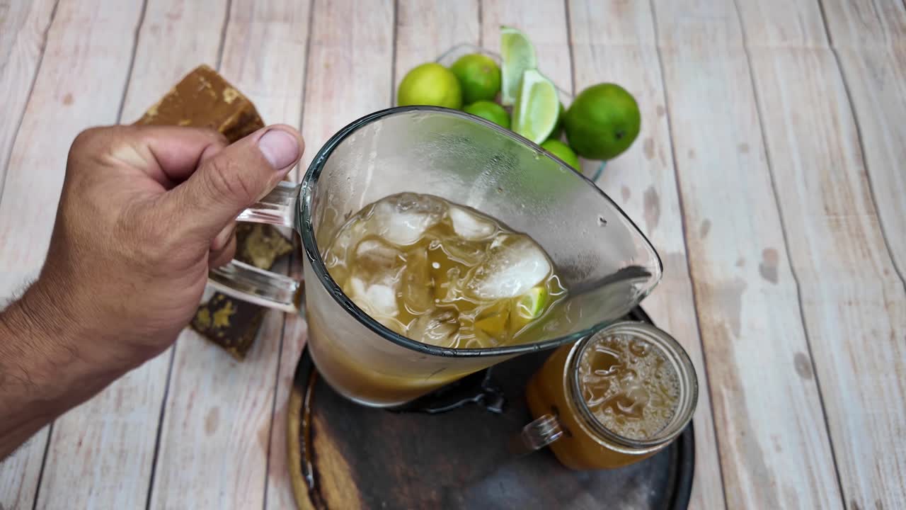 Hand Serving Refreshing Papelón con Limón into Glass. top-down view classic Venezuelan drink with a pitcher, lemons, and panela. Llocal authentic cuisine